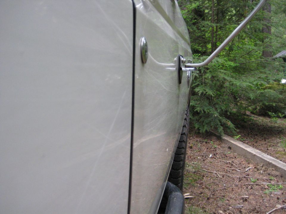 Side view of a light-colored vehicle door and tire in a wooded area.