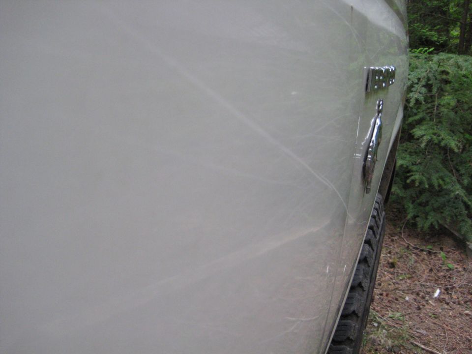 Side view of a scratched light-colored vehicle with a chrome "150" emblem.