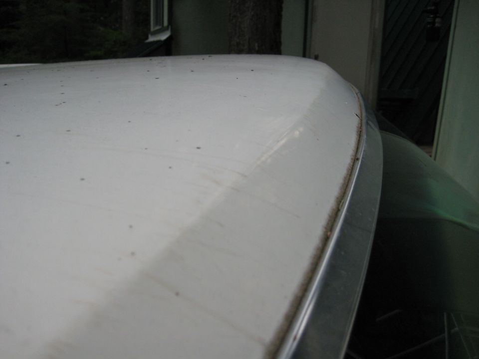 Close-up of a white vehicle roof with chrome trim and dirt, showing another vehicle underneath.