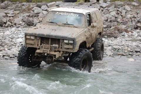 1978 Ford Bronco - Modified SUV navigates a shallow, rocky riverbed. 'Autokrafters' decal on windshield.