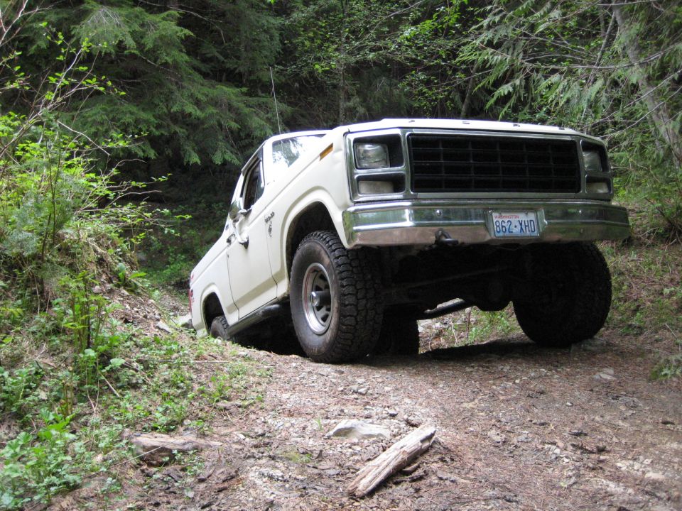 White 1980 Ford Bronco on a dirt trail in a forest.
