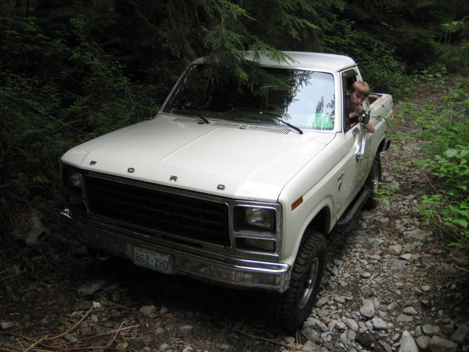 White Ford pickup truck on a rocky trail, driver visible.