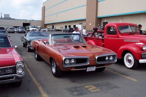 2001 Ford Crown Victoria - A row of classic cars is parked in a lot in front of a large building. The closest car is a copper-colored convertible with a man sitting i…