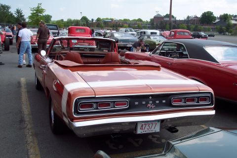 2001 Ford Crown Victoria - A rear view of a copper-colored 1969 Dodge Coronet R/T convertible with white racing stripes parked in an outdoor lot with other vehicles.