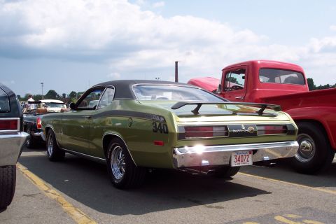 2001 Ford Crown Victoria - The rear view of a green 1970s Plymouth Duster 340 with a black vinyl roof and racing stripes is parked next to a red 1950s pickup truck.