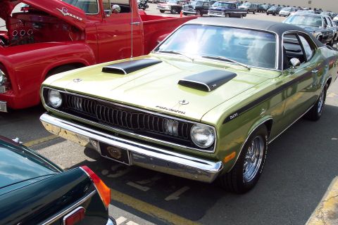 2001 Ford Crown Victoria - A green Plymouth Duster is parked in front of a red Ford pickup truck. The Duster has black hood scoops and black racing stripes along its…