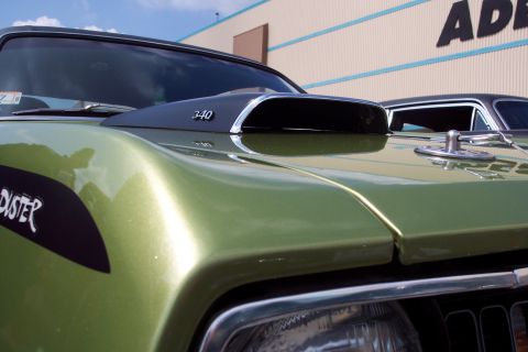 2001 Ford Crown Victoria - A close-up, low-angle shot of the hood and front fender of a green metallic classic car. A black stripe with white lettering reading "DUSTE…