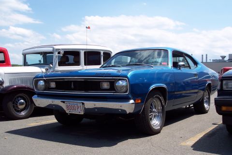 2001 Ford Crown Victoria - A blue 1970 Plymouth Duster is parked in a lot with other vehicles under a partly cloudy sky.
