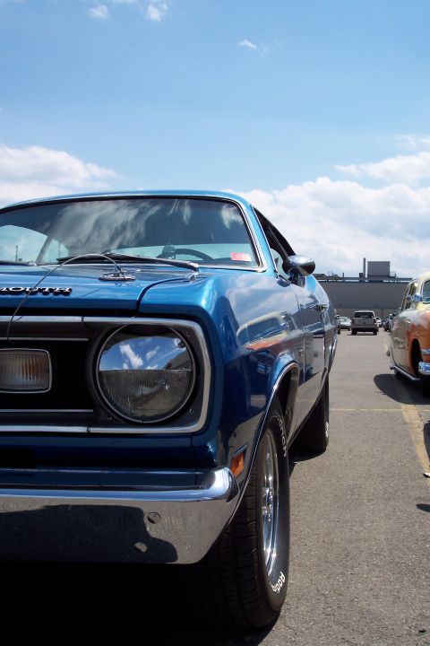 2001 Ford Crown Victoria - A blue Plymouth Duster is parked in a lot next to another car on a sunny day.