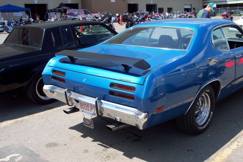 2001 Ford Crown Victoria - The rear quarter panel and trunk of a bright blue classic coupe with a black spoiler are visible. A chrome bumper with dual exhaust pipes a…