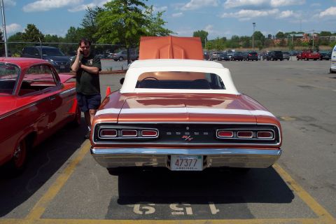 2001 Ford Crown Victoria - The rear of a copper-colored convertible with a white top is shown, parked next to a red car. A man in a dark t-shirt and shorts is standin…