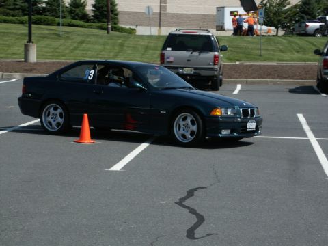 2001 Mercury Grand Marquis - A dark green BMW E36 coupe is seen on an asphalt lot, possibly at an autocross event, with other vehicles in the background.