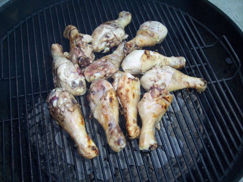 Chicken legs cooking on a grill grate over coals