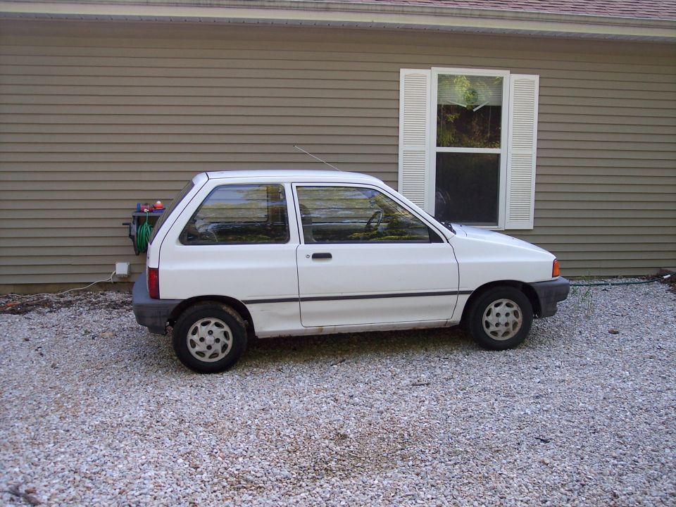 White hatchback car parked on gravel in front of a house, side view