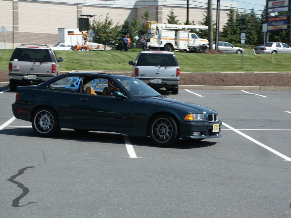 Dark green BMW E36 coupe with racing number 231 on the window, parked in a lot with other vehicles