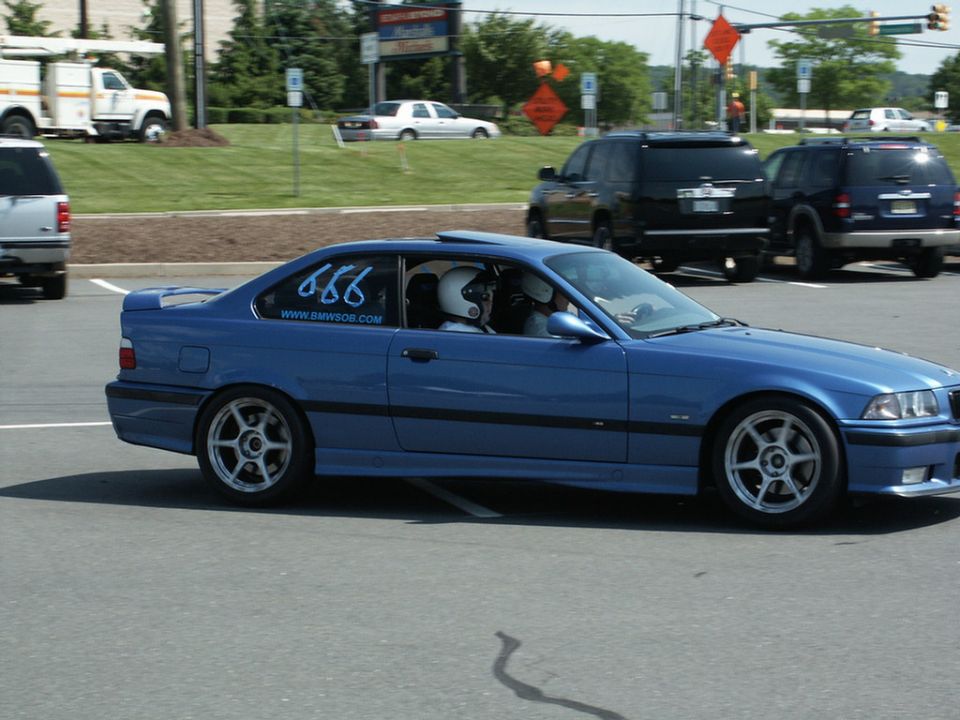 Blue BMW E36 coupe with '666' and 'WWW.BMWSOB.COM' on the window, driver in helmet