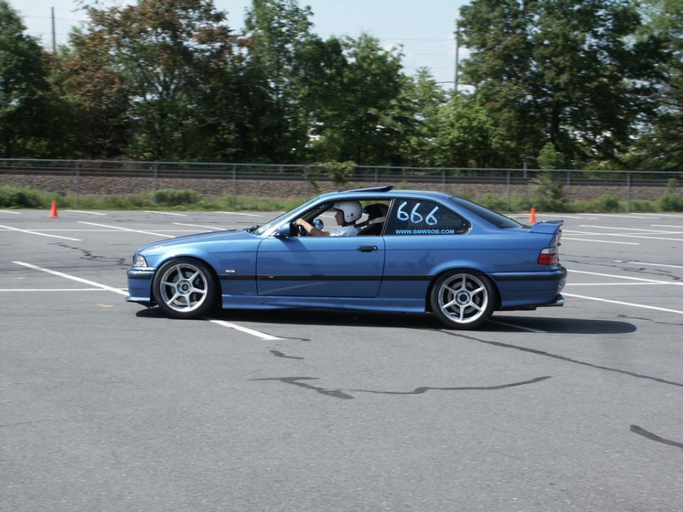 Blue BMW coupe with racing numbers '666' and website on rear window, driving on a paved course