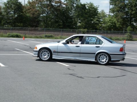 2001 Mercury Grand Marquis - Passenger-side profile of a silver BMW E36 3-Series sedan running an autocross course on a cone-marked parking lot, with the class number 1…