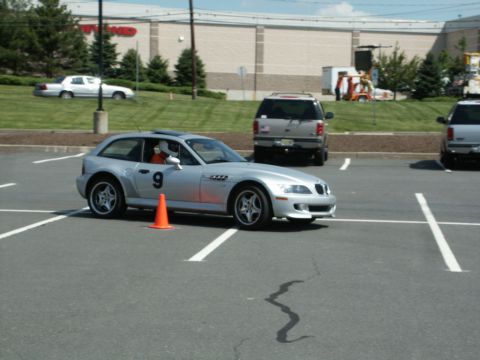 2001 Mercury Grand Marquis - A silver BMW Z3 Coupe navigates a course marked by orange cones in a parking lot, with other vehicles visible in the background.