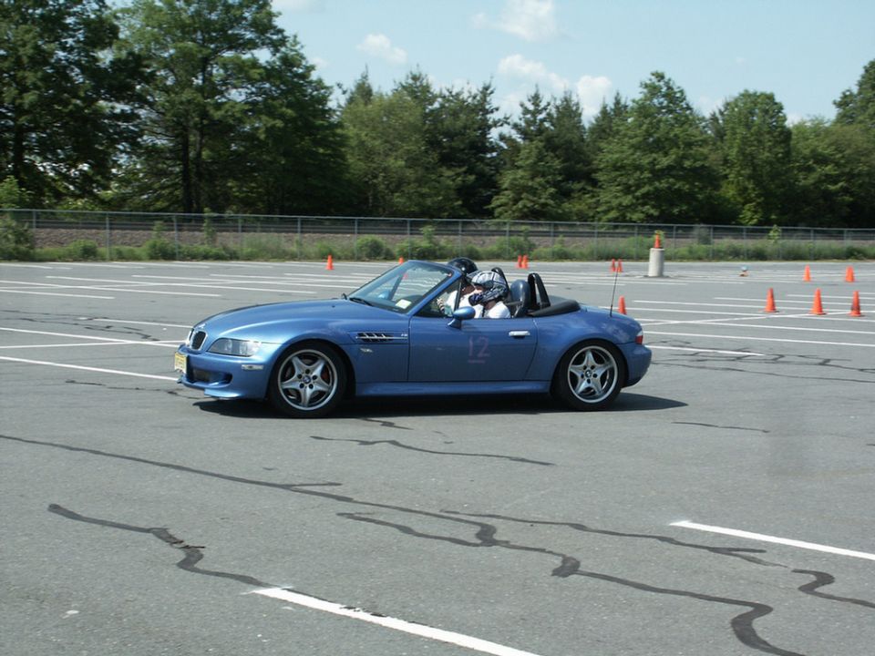 Blue BMW Z3 convertible with racing numbers on door, driving on asphalt track with orange cones