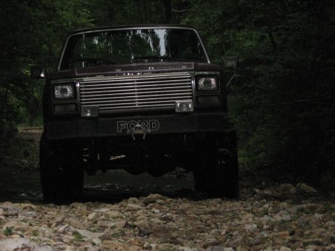 1980 Ford Bronco - A dark brown 1980 Ford Bronco is parked on a rocky path surrounded by trees.