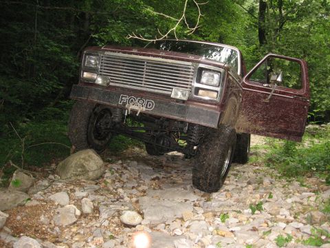 1980 Ford Bronco - This maroon Ford Bronco is navigating a challenging, rocky trail with its driver's door ajar.
