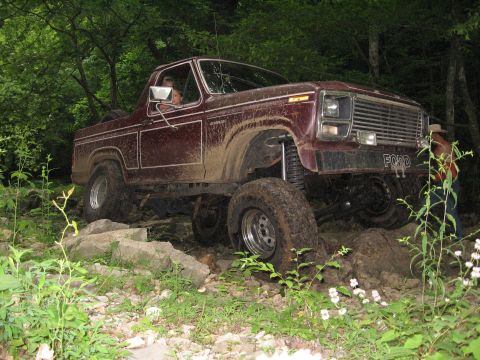 1980 Ford Bronco - This Ford Bronco is shown off-roading on a rocky trail surrounded by trees.