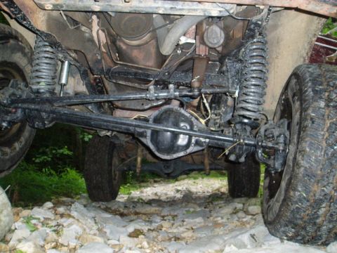 1980 Ford Bronco - The underside of a modified 4x4 vehicle, likely an SUV, showing the front suspension, differential, and tires. The vehicle is on a rocky, u…