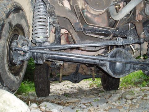 1980 Ford Bronco - Undercarriage view of a 4x4 vehicle, showing the front suspension, steering linkage, and front differential. The vehicle is on a rocky, off…