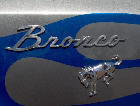 1987 Ford Bronco - A chrome emblem of a rearing horse is positioned below the chrome script text "Bronco" on the side of a vehicle. The vehicle has a two-tone…