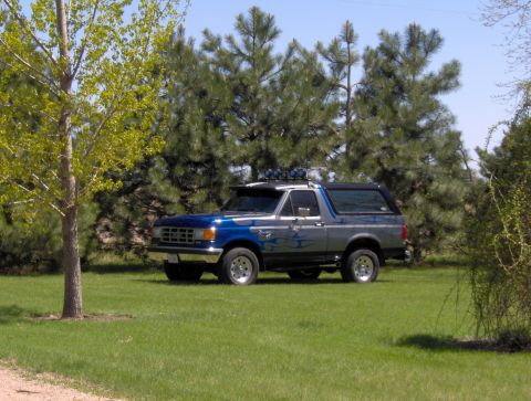 1987 Ford Bronco - A 1987 Ford Bronco is parked on a grassy lawn, surrounded by trees.