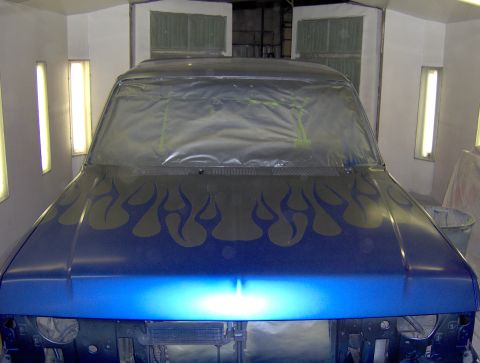 1987 Ford Bronco - A blue SUV with flame decals is being prepped for paint in a booth.