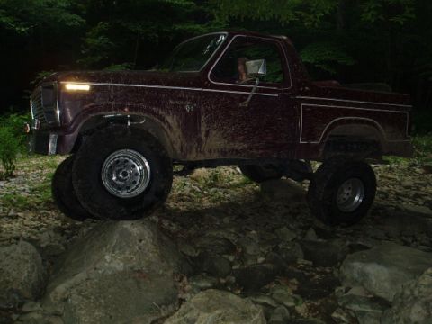 1980 Ford Bronco - This SUV is navigating a rocky trail in a wooded area at night.