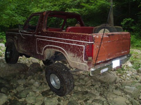 1980 Ford Bronco - A dirty, dark red Ford Bronco is parked on a rocky, wooded trail. The vehicle appears to be a convertible with the top removed, and it is e…