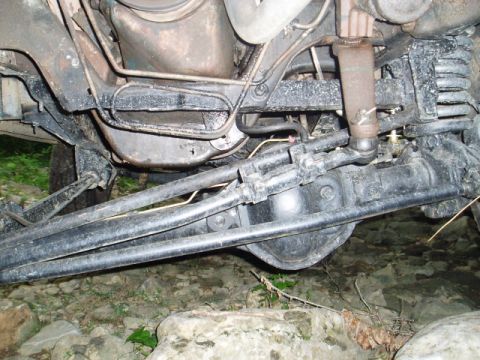 1980 Ford Bronco - Underside view of a vehicle's front axle and suspension system, featuring a differential, steering linkage, and shock absorber. The vehicle…