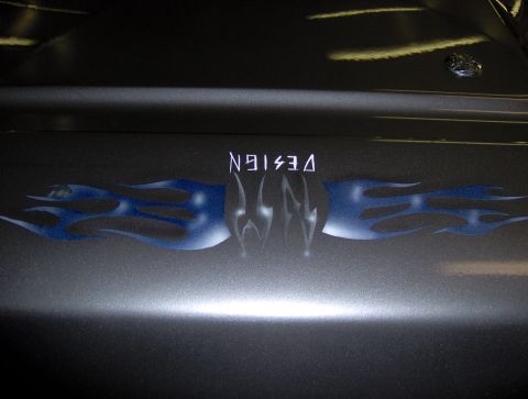 1987 Ford Bronco - A close-up shot of a dark metallic gray vehicle's hood shows a custom airbrushed flame design in blue and white. The word "DESIGN" is stenc…