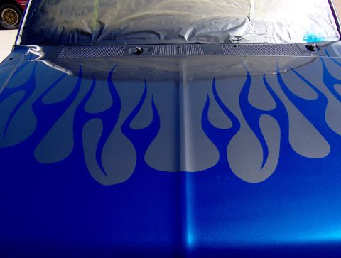 1987 Ford Bronco - The hood of a blue vehicle features a custom flame graphic design in a darker blue or gray. The windshield area is covered with protective…