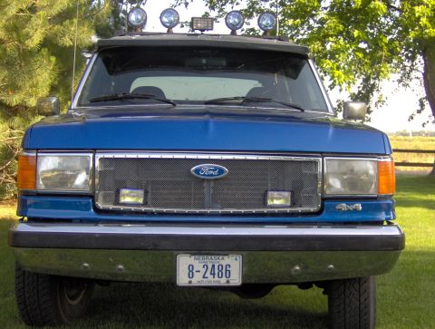 1987 Ford Bronco - Front view of a blue 1987 Ford Bronco with a chrome grille, auxiliary lights on the roof, and a Nebraska license plate. The vehicle is park…