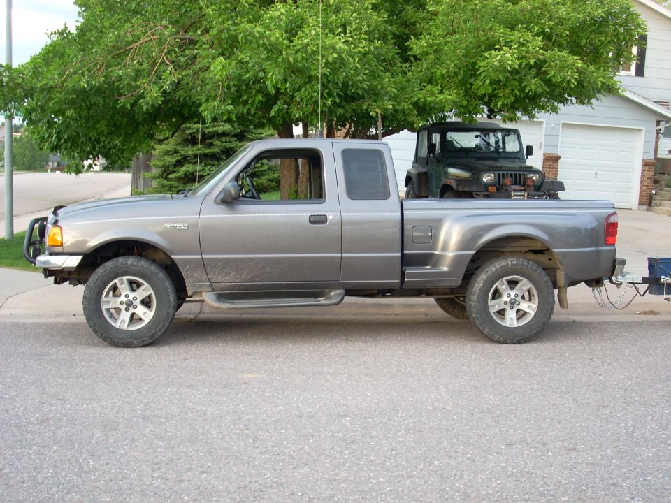 Grey Ford Ranger pickup truck with a Jeep Wrangler in the bed, towing a trailer.