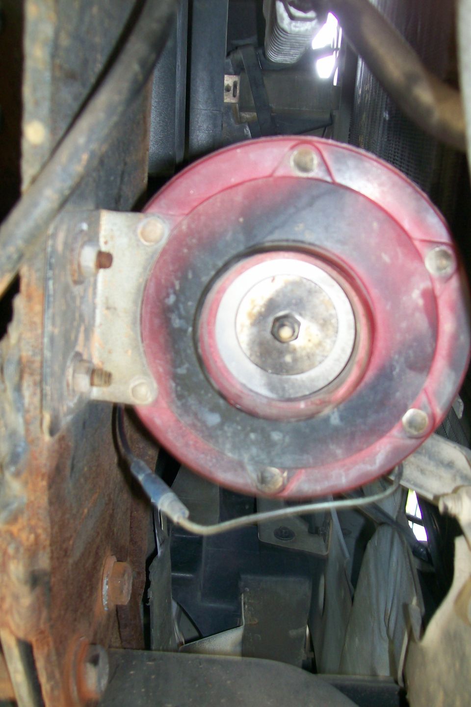 Close-up of a red and black vehicle horn mounted on a rusty bracket.