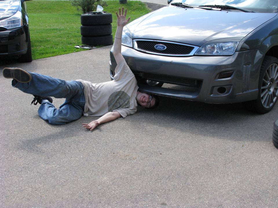 Person lying under a gray Ford Focus with one arm raised.