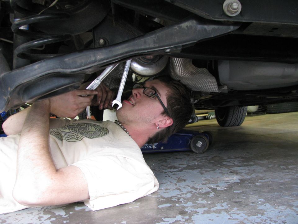 Person working on the suspension of a 2003 Ford Focus with wrenches.