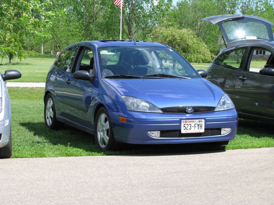 Blue 2003 Ford Focus hatchback with license plate 523-FYH parked on grass.