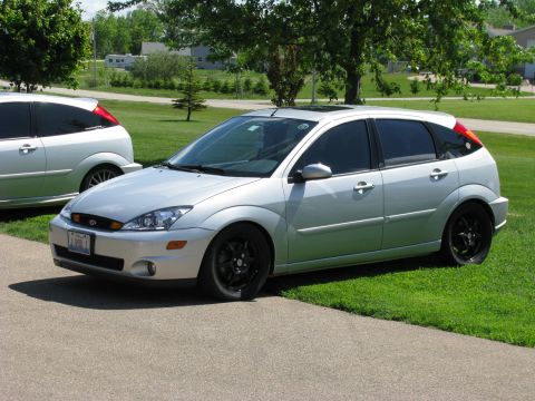 2003 Ford Focus - A silver 2003 Ford Focus hatchback is parked on a paved driveway next to a lawn. The car has tinted windows and black rims.