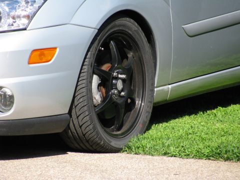 2003 Ford Focus - Close-up front passenger side view of a silver Ford Focus showing the headlight, orange turn signal, black aftermarket wheel, and tire. The…