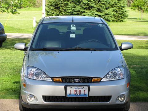 2003 Ford Focus - The front view of a silver 2003 Ford Focus is shown parked on a paved surface with a grassy area and trees in the background. The vehicle h…