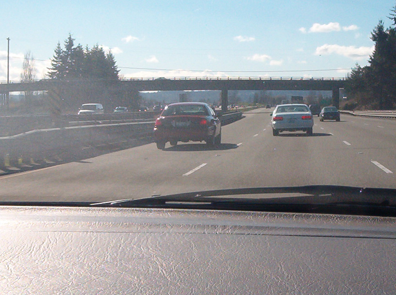 Dashboard view of highway traffic following a dark red sedan toward an overpass