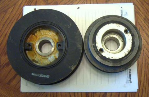 1997 Ford Taurus - Two automotive pulleys are shown on a white paper on a wooden surface. The pulley on the left is larger and appears to be a crankshaft pull…