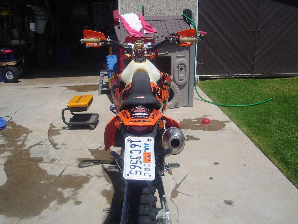 Rear view of orange KTM dirt bike with California plate on concrete driveway
