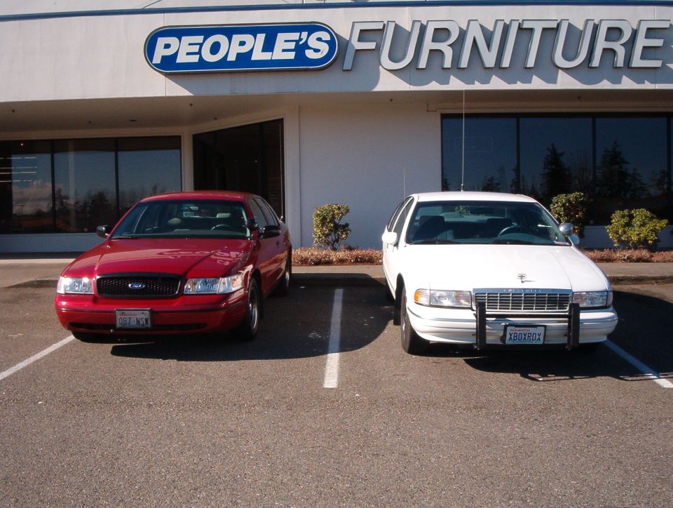 Red Ford sedan and white Chevrolet sedan parked front-facing outside People's Furniture store